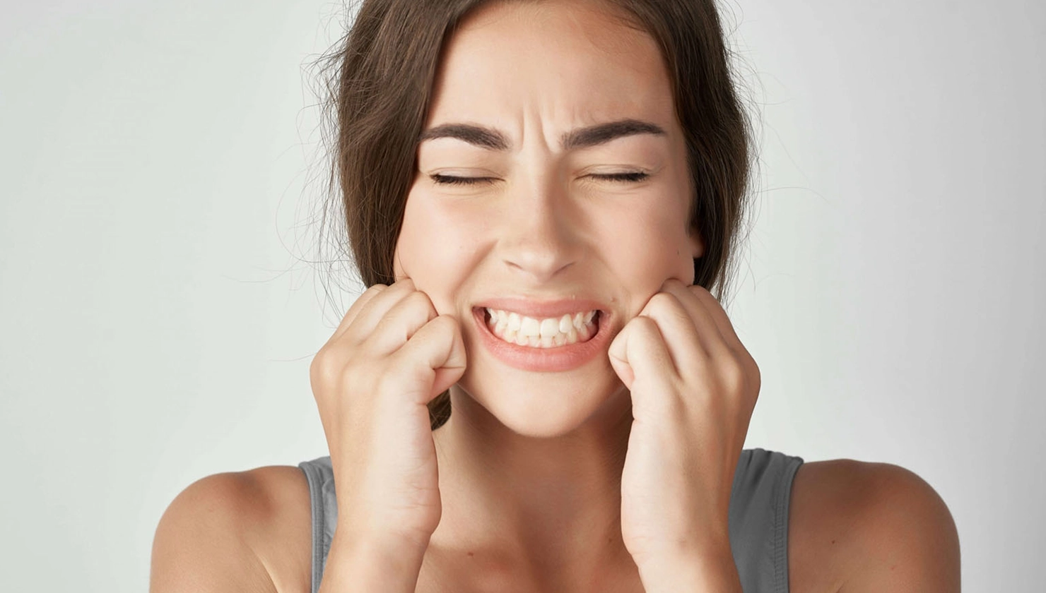 Imatge d'una persona aguantant-se la mandíbula per dolor causat pel bruxisme, afectant la salut dental i l'estètica del somriure.