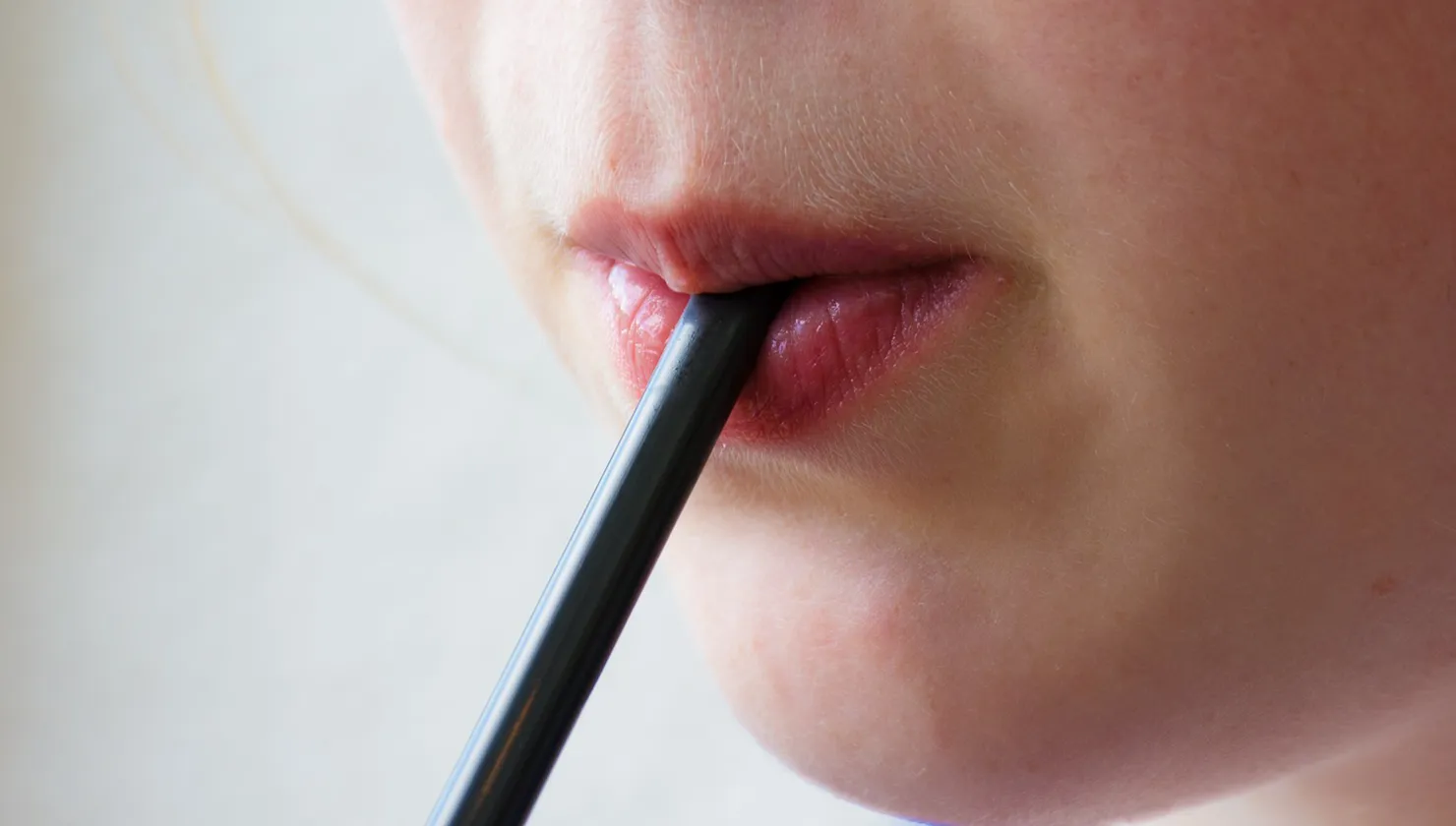 Primer pla d'una boca bevent una beguda freda amb canya, ideal per reduir el contacte del sucre amb les dents