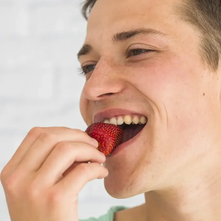 Jove mossegant una maduixa fresca, aliment saludable que enforteix les dents i genives segons Clínica Dental Vilà